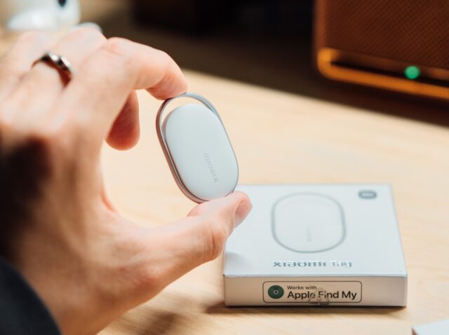 Rastreador inteligente ao lado de smartphone com tela de localização, fundo neutro e iluminação suave.
