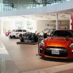 Showroom de concessionária com carro elétrico compacto e picape em exposição, piso polido e iluminação direcionada.