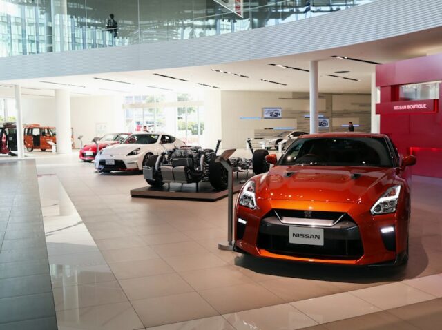 jac-motors-vendas-online-brasil Showroom de concessionária com carro elétrico compacto e picape em exposição, piso polido e iluminação direcionada.