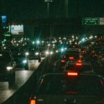Semáforo suspenso sobre avenida movimentada ao anoitecer, com rastros de luz dos veículos ao fundo