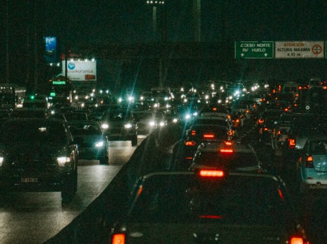 semaforos-inteligentes-ia-transito Semáforo suspenso sobre avenida movimentada ao anoitecer, com rastros de luz dos veículos ao fundo