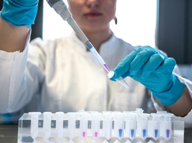 Cientista usando pipeta com tubos de ensaio no laboratório.